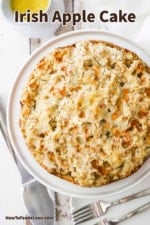 An overhead view of an untouched Irish apple cake with a pie slicer and a couple of forks nearby.