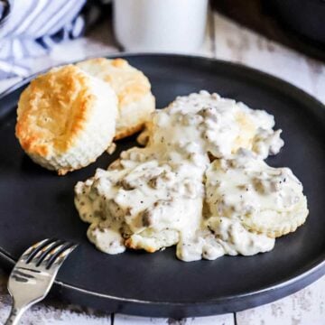 A black circular plate filled with a serving of Southern biscuits and gravy.
