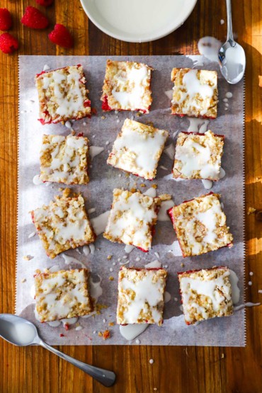An overhead view of three rows of Linzer square sitting on parchment paper on a large wooden cutting board.