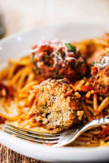 A close-up view of a bowl filled with spaghetti and meatballs with one of the meatballs half eaten.