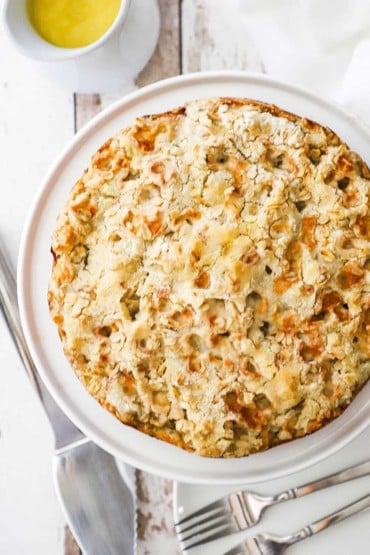 An overhead view of an untouched Irish apple cake with a pie slicer and a couple of forks nearby.
