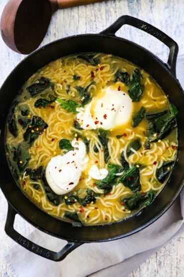 An overhead view of a large black pot filled with ramen with spinach and poached egg.