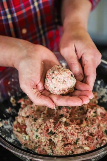A person forming an Italian meatball in his hand over a bowl of the meatball mixture.