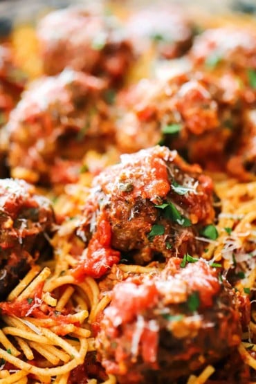A close-up view of numerous cooked meatballs on top of spaghetti with marinara..