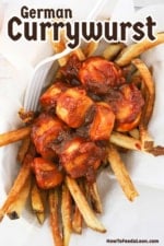 An overhead view of a small food basket filled with a layer of French fries that are topped with sliced German sausage in a currywurst sauce.