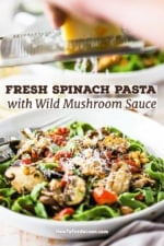 A person grating a block of Parmesan cheese over a pasta bowl filled with spinach linguine with sautéed wild mushrooms and tomatoes.
