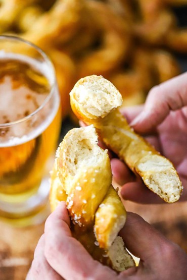 A person holding a freshly baked soft pretzel that has been split open so the inside of the pretzel is visible.