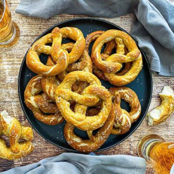 An overhead view of a circular black platter filled with a stack of homemade soft pretzels.