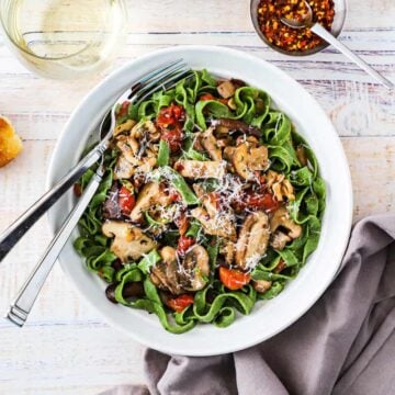 An overhead view of an individual white pasta bowl filled with spinach pasta with wild mushroom sauce.