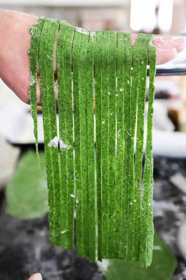 A person holding up homemade spinach pasta that has been cut into linguine.