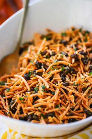 A close-up view of a carrot and raisin salad with homemade curry dressing in a white serving bowl.