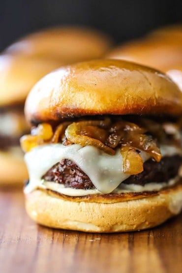 A close-up view of a gourmet beef slider on a toasted bun with a rosemary-garlic aioli sauce, melted provolone cheese, and caramelized onions.