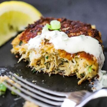 A close-up view of a crab cake topped with a jalapeño remoulade and has been half eaten.