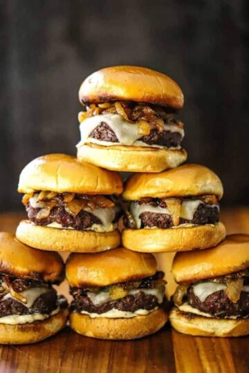 A pyramid stack of gourmet beef sliders on a wooden cutting board.