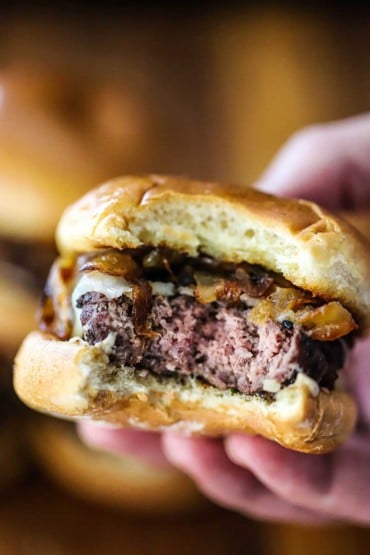 A close-up view of a person holding a beef slider that has a bite taken out of it.