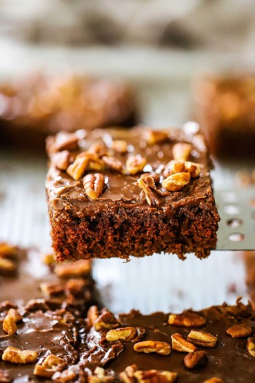 A square slice of Texas sheet cake being raised from the pan with a metal spatula.