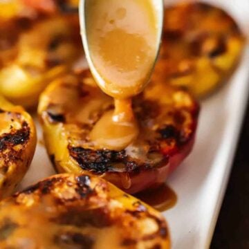 A person using a small spoon to drizzle homemade caramel sauce of a platter filled with grilled peaches.