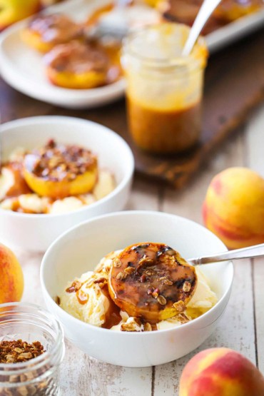 Two white bowls filled with vanilla ice cream and topped with grilled peaches and homemade caramel sauce topped with granola.