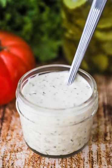 A close-up view of a small glass jar filled with homemade tartar sauce with a spoon stuck into it.