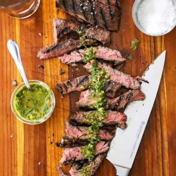 An overhead view of a sous vide skirt steak on a cutting board with half of it cut into strips and topped with homemade chimichurri sauce.