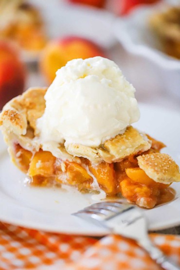 A slice of homemade peach pie sitting on a dessert plate with a large scoop of homemade vanilla cream sitting on top, just starting to melt.
