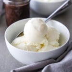 A close-up view of a white dessert bowl filled with several scoops of homemade vanilla ice cream.