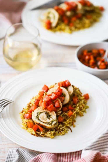 Two white dinner plates filled with a helping of pesto-stuffed chicken with tomato relish that has been sliced and placed on rice pilaf.