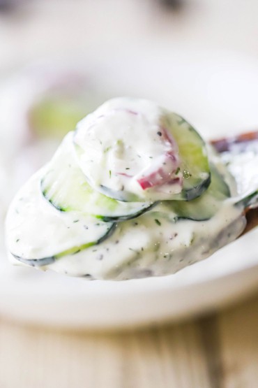 A close-up view of a wooden spoon filled with a pile of creamy tzatziki cucumber salad.