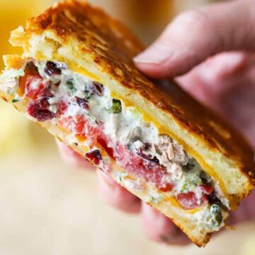 A close-up view of a person holding up a tuna melt sandwich that has been sliced in half.