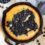 An overhead view of a black cast-iron skillet that is full of an untouched blueberry cobbler with crusty lightly browned edges.