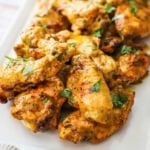 A close-up view of grilled curry chicken wings topped with chopped cilantro on a white platter.