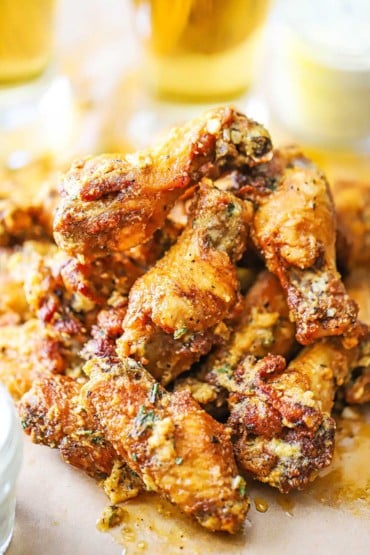 A pile of garlic Parmesan wings sitting on a piece of brown paper with two glassed of beer in the background.