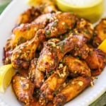 A close-up view of Italian-style wings with chunks of garlic sprinkled over the top and lemon wedges on the side.
