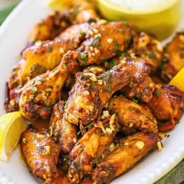 A close-up view of Italian-style wings with chunks of garlic sprinkled over the top and lemon wedges on the side.