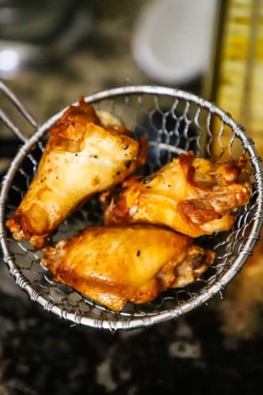 A person holding up a metal kitchen spider with three deep-fried chicken wings in it.