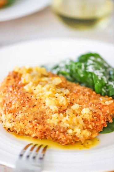 A close-up view of an almond crusted cod with orange sauce next to a small pile of a spinach salad on a white dinner plate.