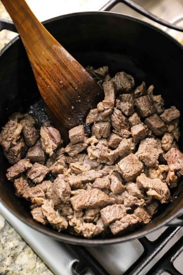 An overhead view of a black pot filled with chunks of chuck roast that have been browned in olive oil.