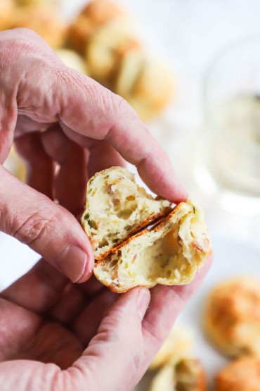 A person holding a parmesan bacon gourgere that has been split in two so the puffed interior is visible.