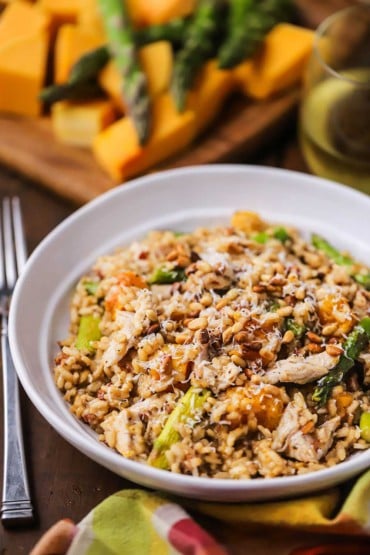 A straight-on view of a shallow white dinner bowl filled with risotto with left-over turkey, roasted butternut squash, and asparagus.