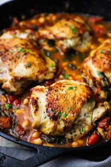 A close-up view of Tuscan chicken with white beans and spinach in a large black cast-iron skillet.