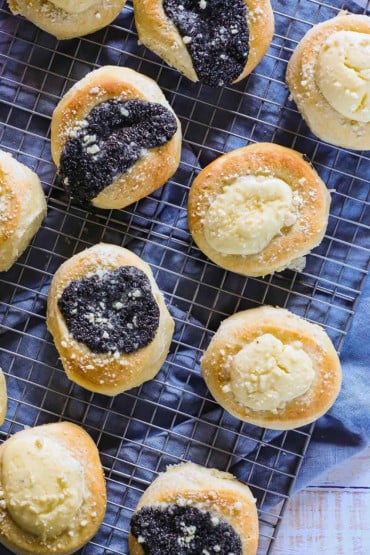 An overhead view of poppyseed and cream cheese filled kolaches sitting on a baking rack with a blue linen napkin underneath it.