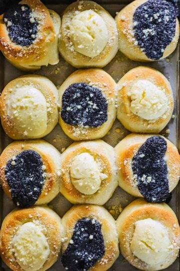 An overhead view of a baking pan filled with freshly baked kolaches topped with poppyseed filling and cream cheese filling.