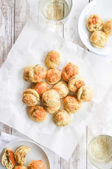 An overhead view of a pile of bacon parmesan gourgeres on a square white wax piece of paper.