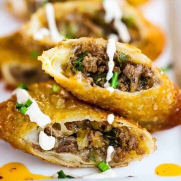 A close-up view of a row of Philly cheesesteak egg rolls that have been split in half and sitting on a white platter.