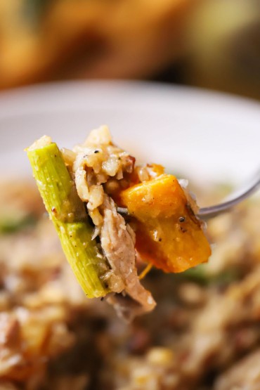 A dinner fork that has pierced roasted asparagus, left-over turkey, and butternut squash, and is being raised up.