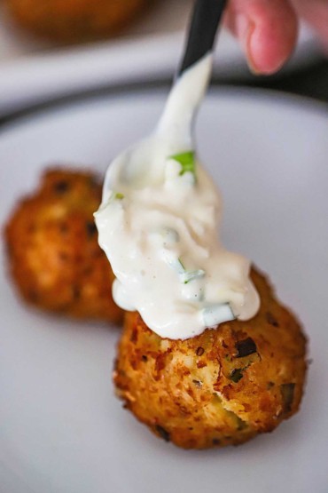A person spooning on white remoulade onto a fried Southern crab beignet.