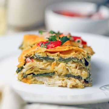 A straight-on view of a square slice of green enchilada casserole topped with chopped tomatoes and cilantro.