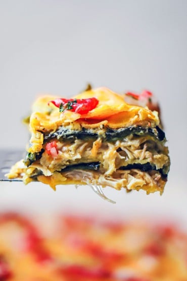 A square slice of a green enchilada casserole being raised up on a metal spatula.