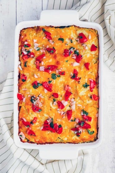 An overhead view of a nine by thirteen white casserole dish filled with a tortillas, cheese, roasted peppers, and enchilada sauce, baked until golden.