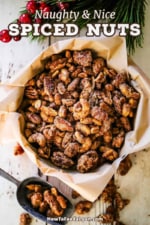 An overhead view of spiced nuts that are in a large tin that is lined with brown paper and a scooper next to it filled with more of the spiced nuts.
